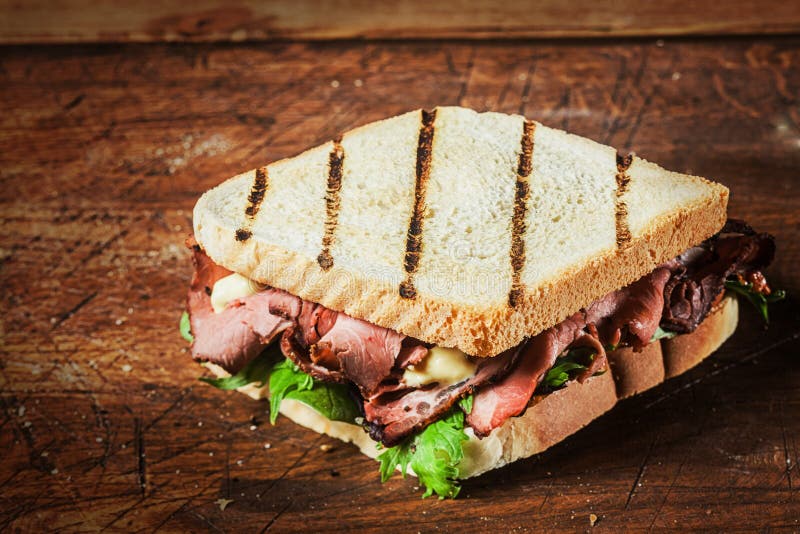 Grilled sandwich from a BBQ with rare roast beef and fresh leafy green herbs on a rustic wooden table. Grilled sandwich from a BBQ with rare roast beef and fresh leafy green herbs on a rustic wooden table