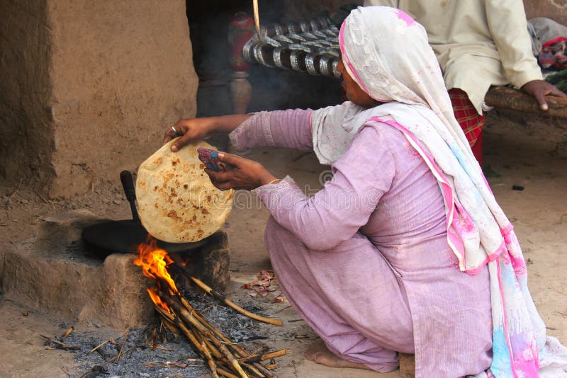 A villager woman is making bread on the heat of wooden fire. This is the traditional way of making chapatti in the villages of Pakistan, where other facilities are not available and people have to burn woods to cook the food. A villager woman is making bread on the heat of wooden fire. This is the traditional way of making chapatti in the villages of Pakistan, where other facilities are not available and people have to burn woods to cook the food.