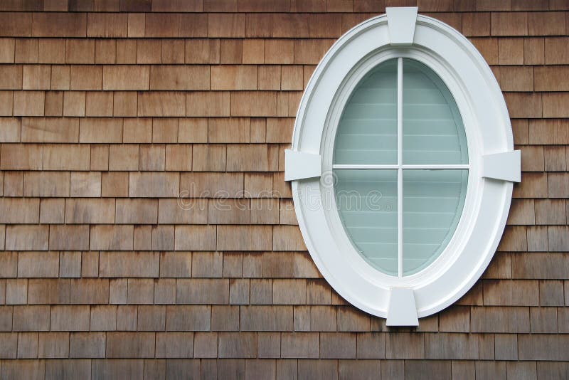 An oval window on the side of a house with shingles. An oval window on the side of a house with shingles.