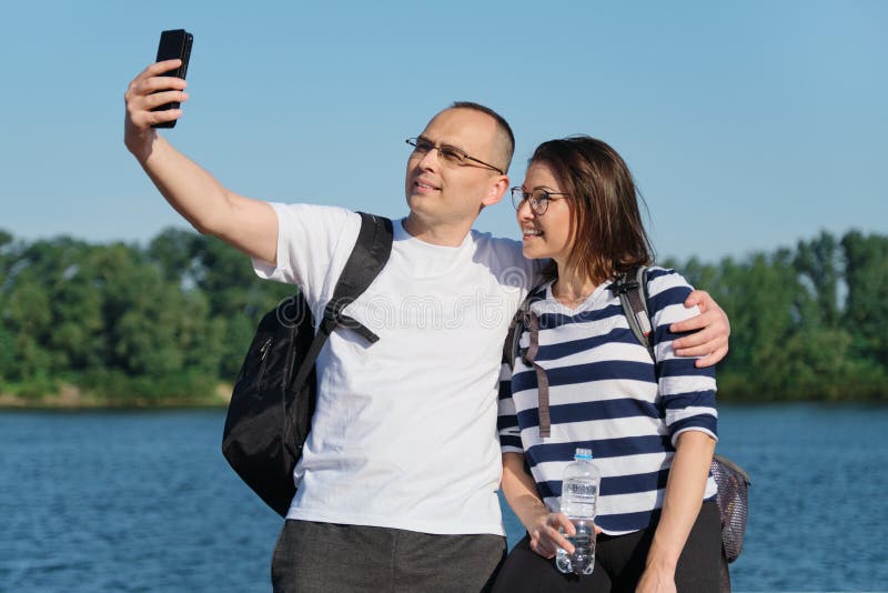 Ωριμάστε το ευτυχές ζεύγος που παίρνει selfie τη φωτογραφία στο τηλέφωνο, άνθρωποι που χαλαρώνουν κοντά στον ποταμό στο πάρκο θερ στοκ εικόνα