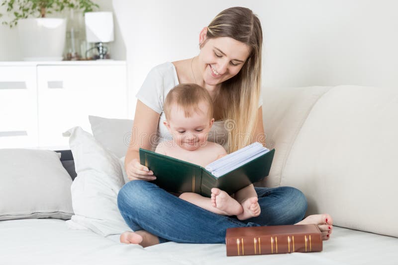 Όμορφες νέες ιστορίες μητέρων χαμόγελου readin στο αγοράκι της στο κρεβάτι στοκ εικόνα Όμορφες νέες ιστορίες μητέρων χαμόγελου readin στο αγοράκι της στο κρεβάτι στοκ εικόνα