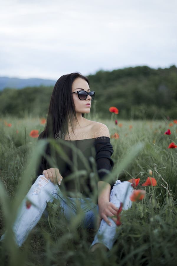 Όμορφη γυναίκα brunette στα γυαλιά ηλίου και τα μοντέρνα ενδύματα που κάθεται μεταξύ στις κόκκινες παπαρούνες στοκ εικόνες με δικαίωμα ελεύθερης χρήσης Όμορφη γυναίκα brunette στα γυαλιά ηλίου και τα μοντέρνα ενδύματα που κάθεται μεταξύ στις κόκκινες παπαρούνες στοκ εικόνες με δικαίωμα ελεύθερης χρήσης