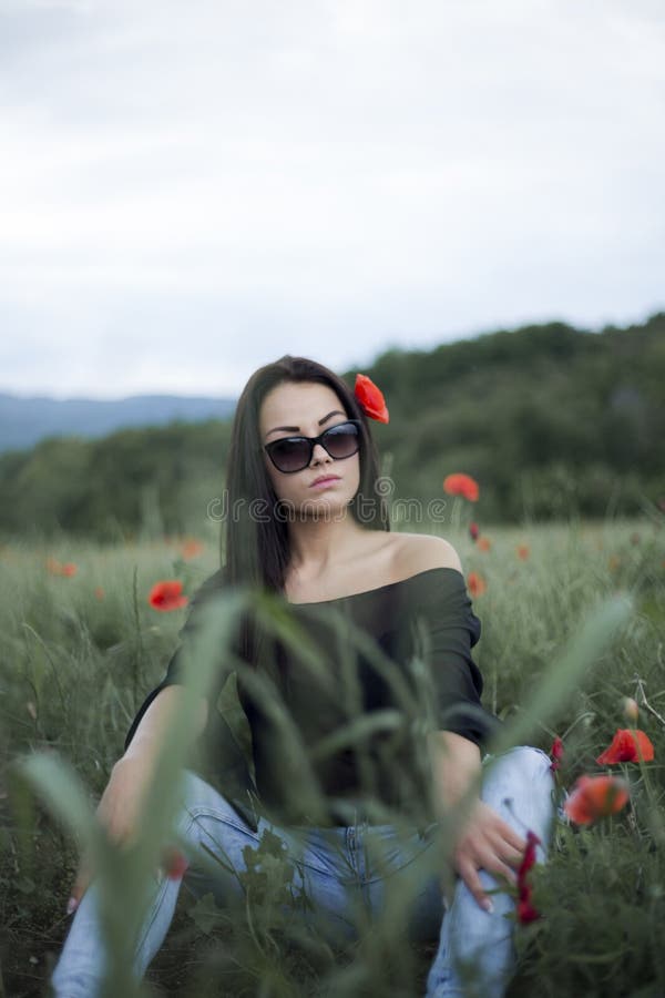 Όμορφη γυναίκα brunette στα γυαλιά ηλίου και τα μοντέρνα ενδύματα που κάθεται μεταξύ στις κόκκινες παπαρούνες στοκ εικόνα με δικαίωμα ελεύθερης χρήσης Όμορφη γυναίκα brunette στα γυαλιά ηλίου και τα μοντέρνα ενδύματα που κάθεται μεταξύ στις κόκκινες παπαρούνες στοκ εικόνα με δικαίωμα ελεύθερης χρήσης