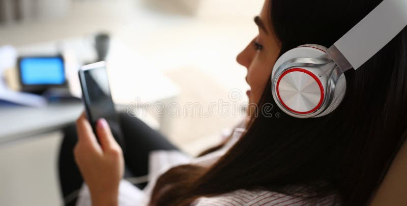 Young beautiful woman headphones holds smartphone in hand using at home costs about sofa. Verifies internal information its financial advertising freedom makes money level transfer contractor concept. Young beautiful woman headphones holds smartphone in hand using at home costs about sofa. Verifies internal information its financial advertising freedom makes money level transfer contractor concept