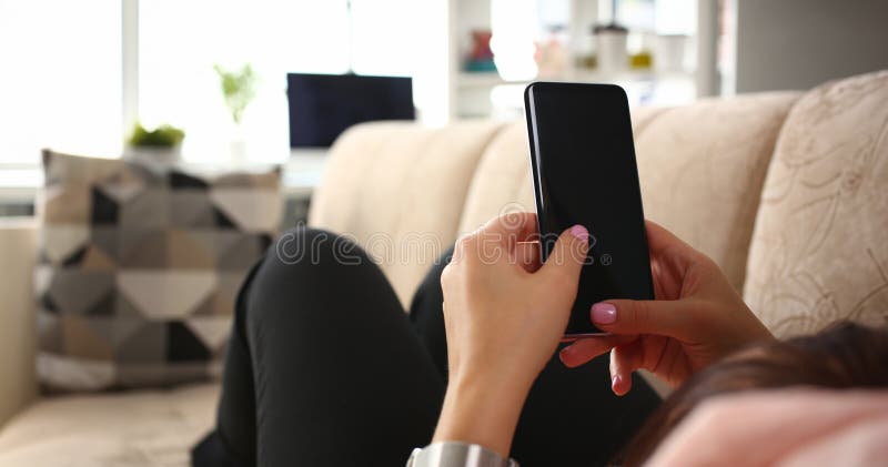 Young beautiful woman holds smartphone in hand using at home costs about sofa. Verifies internal information its financial advertising freedom makes money level transfer to contractor concept. Young beautiful woman holds smartphone in hand using at home costs about sofa. Verifies internal information its financial advertising freedom makes money level transfer to contractor concept