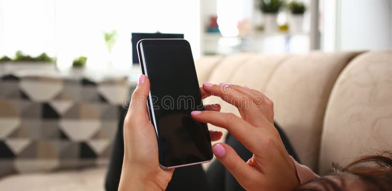 Young beautiful woman holds smartphone in hand using at home costs about sofa. Verifies internal information its financial advertising freedom makes money level transfer to contractor concept. Young beautiful woman holds smartphone in hand using at home costs about sofa. Verifies internal information its financial advertising freedom makes money level transfer to contractor concept