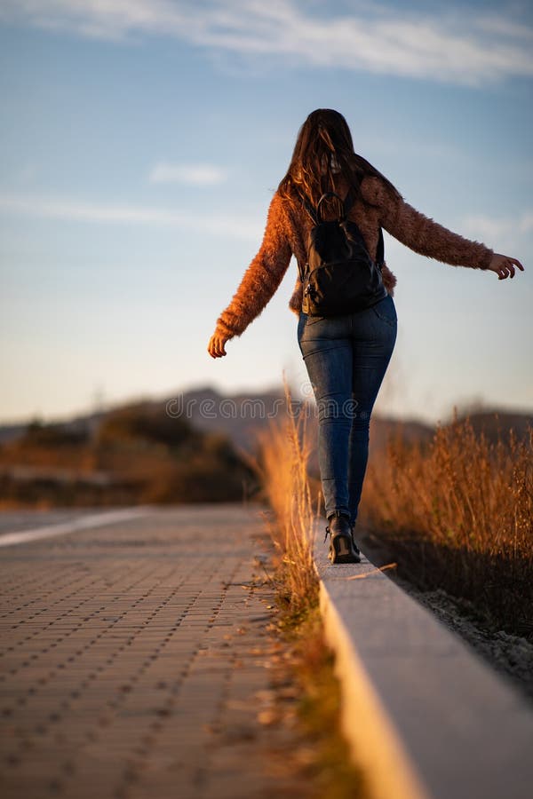 Όμορφη γυναίκα που περπατά και που ισορροπεί στη συγκράτηση ή το κράσπεδο οδών κατά τη διάρκεια του ηλιοβασιλέματος