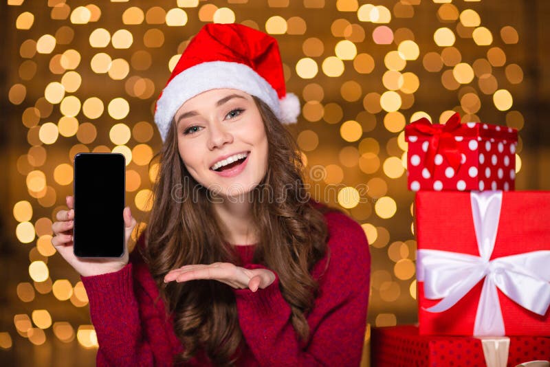 Όμορφη γυναίκα στο καπέλο santa που παρουσιάζει στο τηλέφωνο κυττάρων κενή οθόνη στοκ φωτογραφία με δικαίωμα ελεύθερης χρήσης Όμορφη γυναίκα στο καπέλο santa που παρουσιάζει στο τηλέφωνο κυττάρων κενή οθόνη στοκ φωτογραφία με δικαίωμα ελεύθερης χρήσης