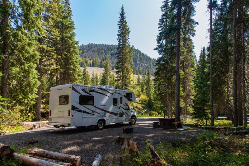 JASPER, CANADA - Jun 03, 2019: Beautiful campsite in the forest on a lovely sunny day. There is an RV and a wooden bench and a mountain in the background. JASPER, CANADA - Jun 03, 2019: Beautiful campsite in the forest on a lovely sunny day. There is an RV and a wooden bench and a mountain in the background
