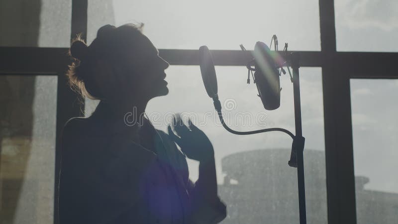 όμορφη κινηματογραφική φωτογραφία μιας νεαρής τραγουδίστριας με μικρόφωνο στο στούντιο.