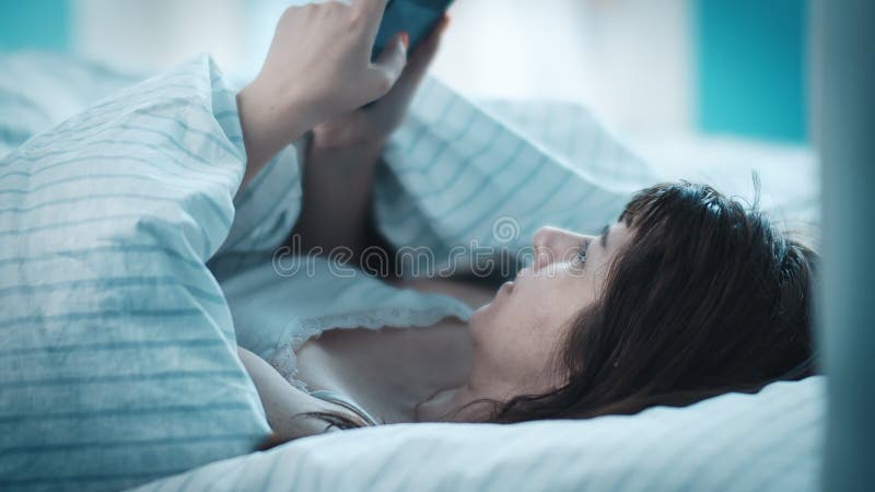 όμορφη μελαχρινή γυναίκα βάζει κεφάλι σε ένα μαξιλάρι στο κρεβάτι το πρωί και χρησιμοποιεί το τηλέφωνο διαβάζοντας κάποιες πληροφο απόθεμα βίντεο