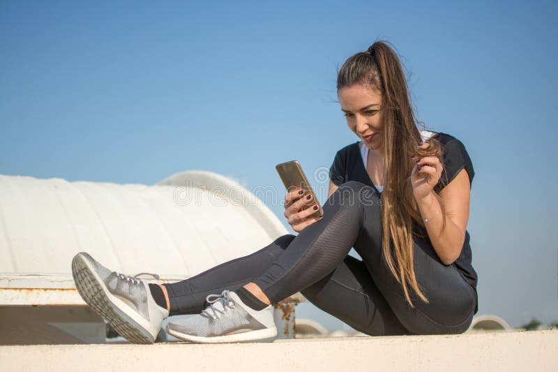 Beautiful young fit woman in sportswear using mobile phone while sitting on rooftop. Beautiful young fit woman in sportswear using mobile phone while sitting on rooftop