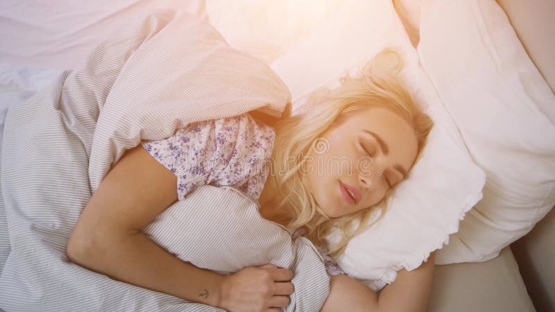 όμορφη νεαρή γυναίκα με ξανθά μαλλιά ξαπλωμένη στο άνετο κρεβάτι κάτω από ζεστή κουβέρτα απόθεμα βίντεο