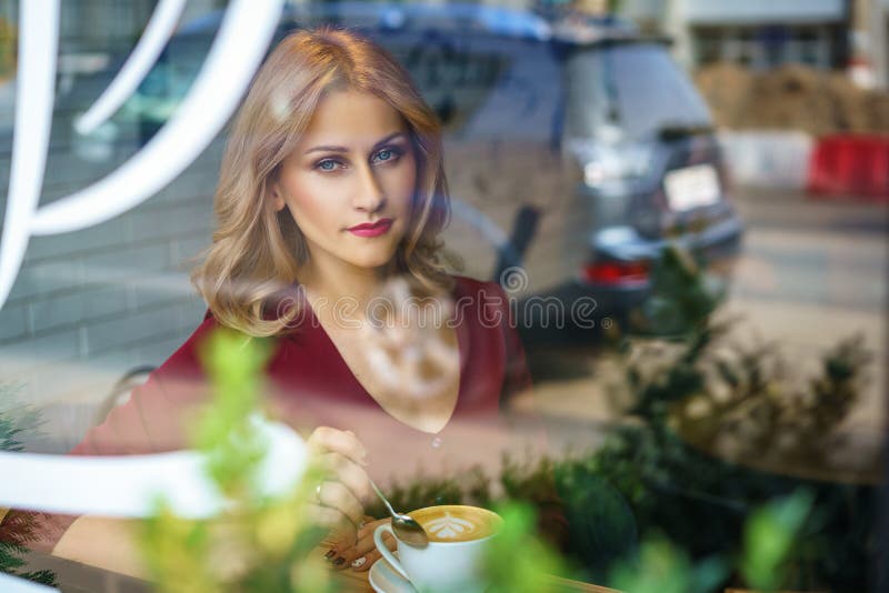 Όμορφη συνεδρίαση γυναικών από το παράθυρο σε έναν καφέ κατανάλωσης καφέδων στοκ εικόνα με δικαίωμα ελεύθερης χρήσης Όμορφη συνεδρίαση γυναικών από το παράθυρο σε έναν καφέ κατανάλωσης καφέδων στοκ εικόνα με δικαίωμα ελεύθερης χρήσης