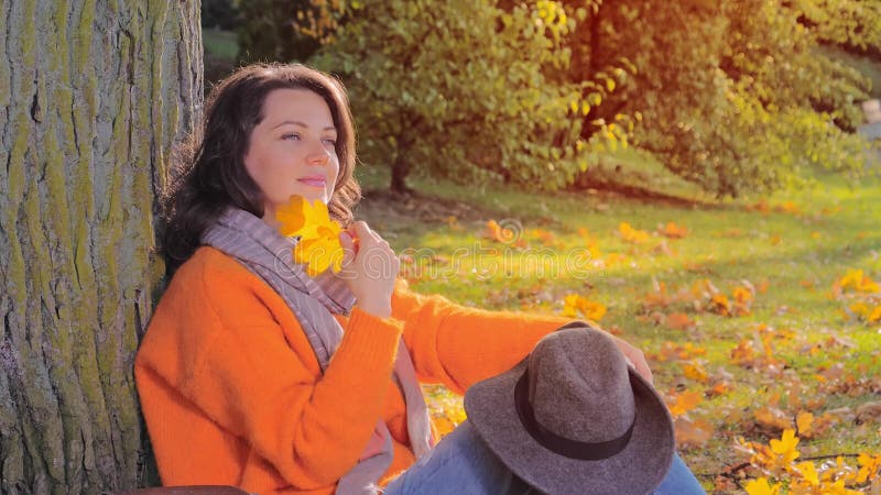 Όμορφη φθινοπωρινή γυναίκα με πορτοκαλί φύλλο στο πάρκο