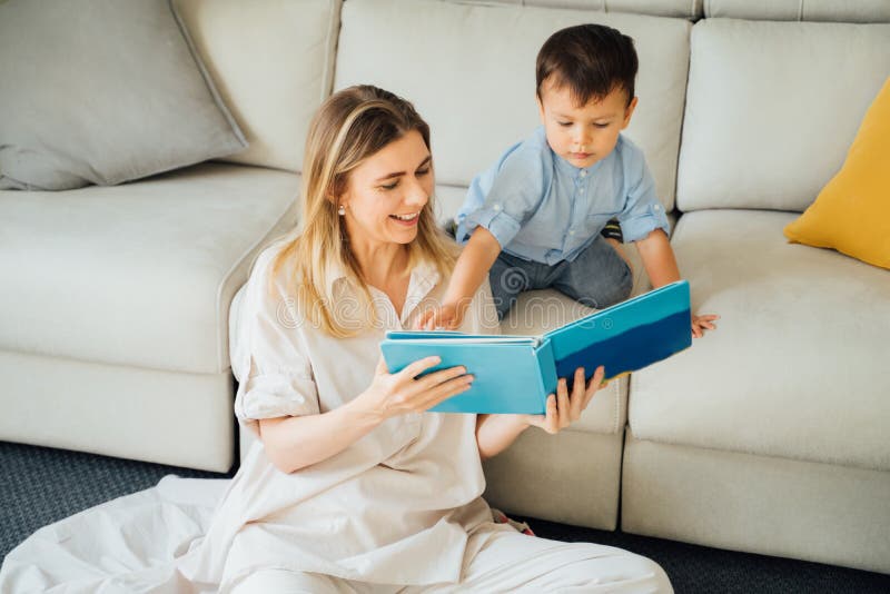 Reading with kid. Beautiful smiling blond women holding book playing with small 2 years old boy. Relaxed time with family. upbringing and education of the child. Family time at home. Sunny liningroom. Reading with kid. Beautiful smiling blond women holding book playing with small 2 years old boy. Relaxed time with family. upbringing and education of the child. Family time at home. Sunny liningroom