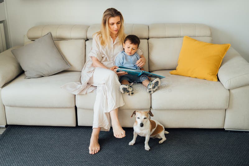 Family time at home. Beautiful smiling blond woman, 2 yers old boy and dog together in living room reading books. Happy relaxed moment. upbringing and education of the child. Horizontal composition. Family time at home. Beautiful smiling blond woman, 2 yers old boy and dog together in living room reading books. Happy relaxed moment. upbringing and education of the child. Horizontal composition