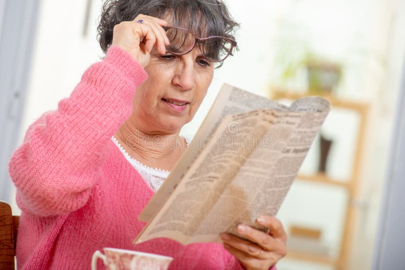 Όμορφη ώριμη γυναίκα brunette που ντύνει στη ρόδινη εφημερίδα ανάγνωσης στοκ εικόνες Όμορφη ώριμη γυναίκα brunette που ντύνει στη ρόδινη εφημερίδα ανάγνωσης στοκ εικόνες