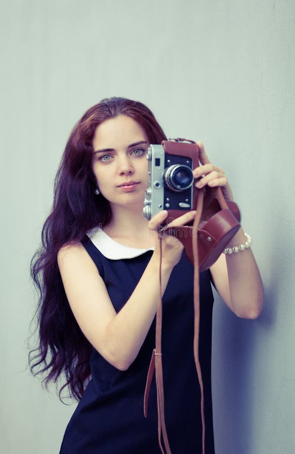 Όμορφο brunette με τη μακρυμάλλη εξέταση τη κάμερα και το κράτημα στα χέρια της εκλεκτής ποιότητας κάμερας Ζωηρόχρωμη φωτογραφία στοκ εικόνα