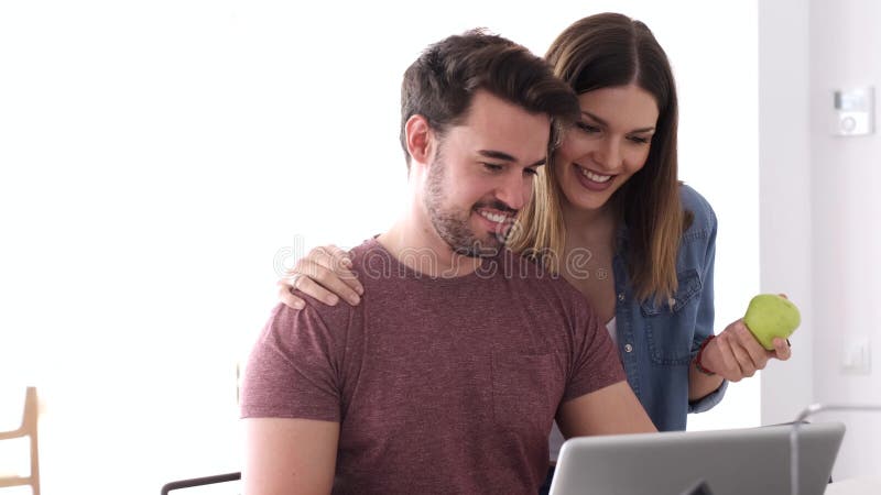 Όμορφο καλό νέο ζεύγος χρησιμοποιώντας το lap-top τους και μιλώντας στην κουζίνα στο σπίτι απόθεμα βίντεο
