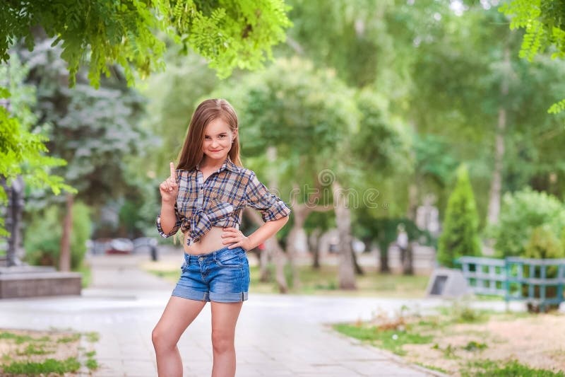 Όμορφο κορίτσι με το χαμόγελο και να κρατήσει ψηλά του αντίχειρα Ένα κορίτσι σε ένα πουκάμισο καρό και κοντά σορτς τζιν Η έννοια στοκ εικόνες Όμορφο κορίτσι με το χαμόγελο και να κρατήσει ψηλά του αντίχειρα Ένα κορίτσι σε ένα πουκάμισο καρό και κοντά σορτς τζιν Η έννοια στοκ εικόνες