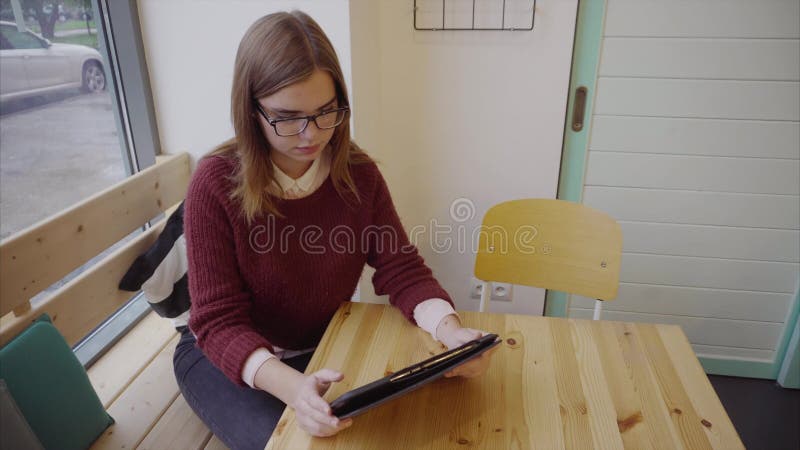Όμορφο κορίτσι σπουδαστών που χρησιμοποιεί το τηλέφωνο ταμπλετών στον καφέ