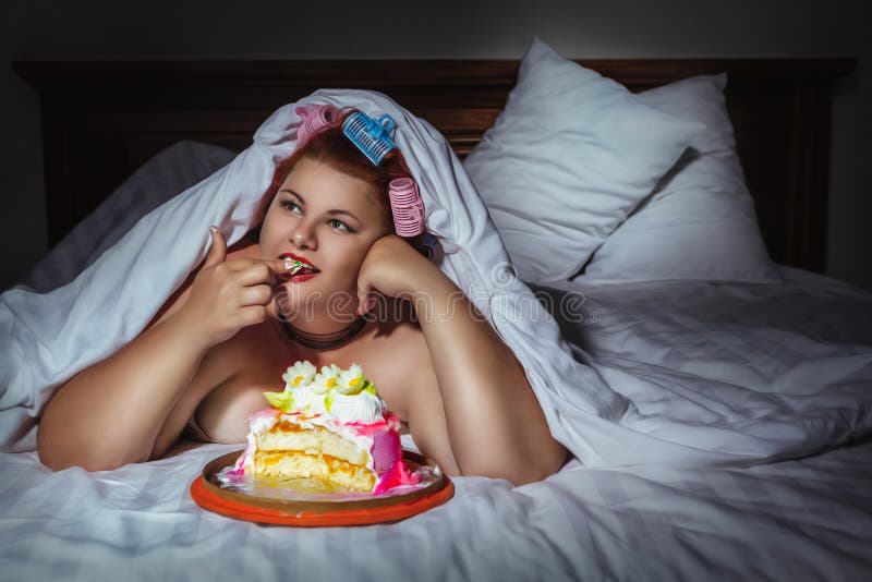 Portrait of beautiful plus size curly red hair young woman hiding under the blanket and eating sweet pastry in bed. Portrait of beautiful plus size curly red hair young woman hiding under the blanket and eating sweet pastry in bed