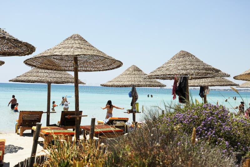 Όμορφο παραθαλάσσιο θέρετρο με τις ομπρέλες αχύρου σε έναν μπλε ουρανό και άσπρα σύννεφα Στο υπόβαθρο μερικοί άνθρωποι που έχουν στοκ φωτογραφία με δικαίωμα ελεύθερης χρήσης Όμορφο παραθαλάσσιο θέρετρο με τις ομπρέλες αχύρου σε έναν μπλε ουρανό και άσπρα σύννεφα Στο υπόβαθρο μερικοί άνθρωποι που έχουν στοκ φωτογραφία με δικαίωμα ελεύθερης χρήσης