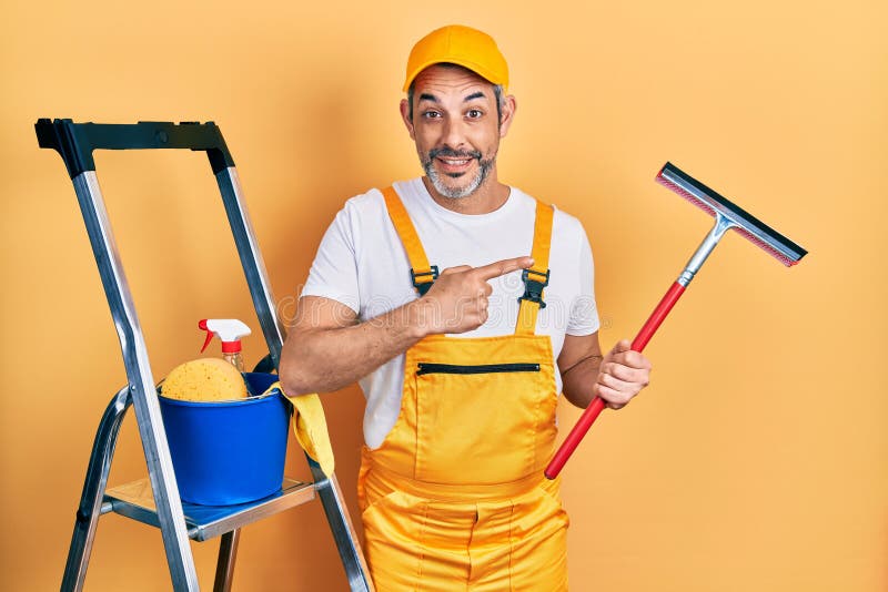 όμορφος μεσήλικας άνδρας με γκρι μαλλιά με στολή από γυαλί καθαριστικό και συμφιλιωμένος χαμογελαστός χαρούμενος που δείχνει με το χέρι και το δάχτυλο