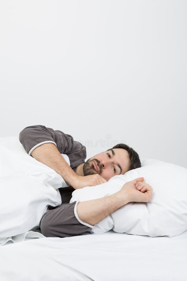 Man with beard lying in a bed with white bedding. Man with beard lying in a bed with white bedding