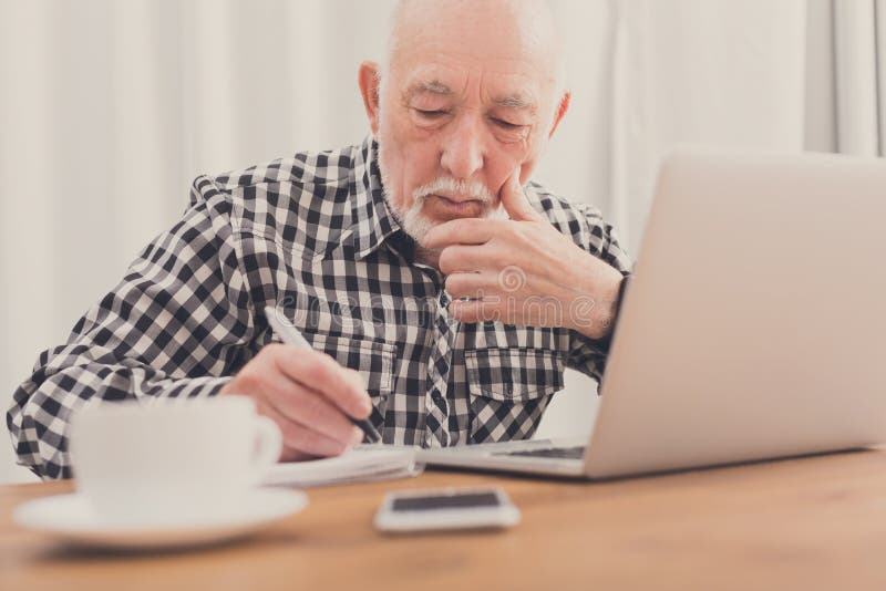 Ώριμο άτομο χρησιμοποιώντας το lap-top και γράφοντας στο σημειωματάριο στοκ φωτογραφία Ώριμο άτομο χρησιμοποιώντας το lap-top και γράφοντας στο σημειωματάριο στοκ φωτογραφία