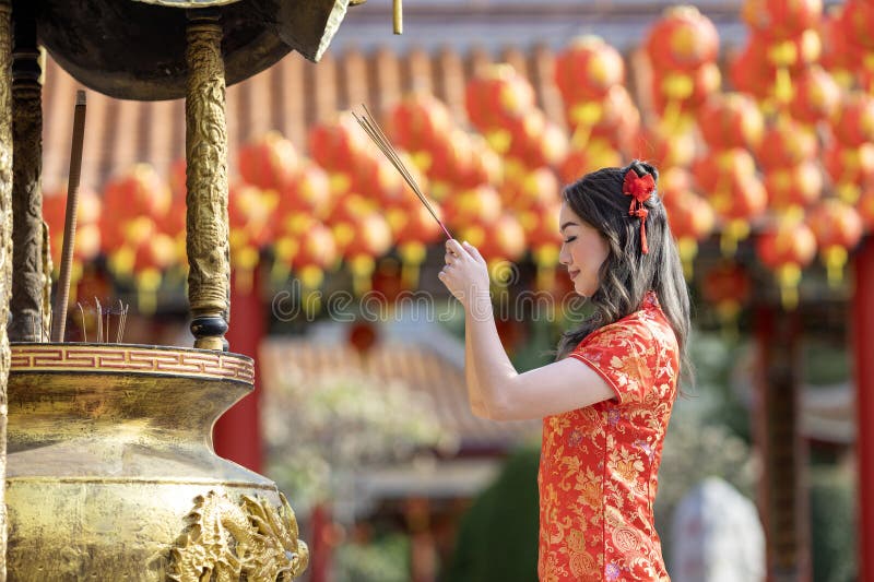 азиатка в красном платье cheongsam qipao предлагает благовоние родовому богу внутри китайского буддистского храма во время лунного стоковое фото