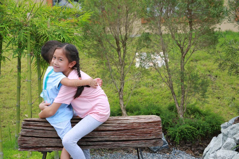 азиатская девочка, обнимающая маленького мальчика, сидя на деревянной скамейке в парке стоковое фото rf