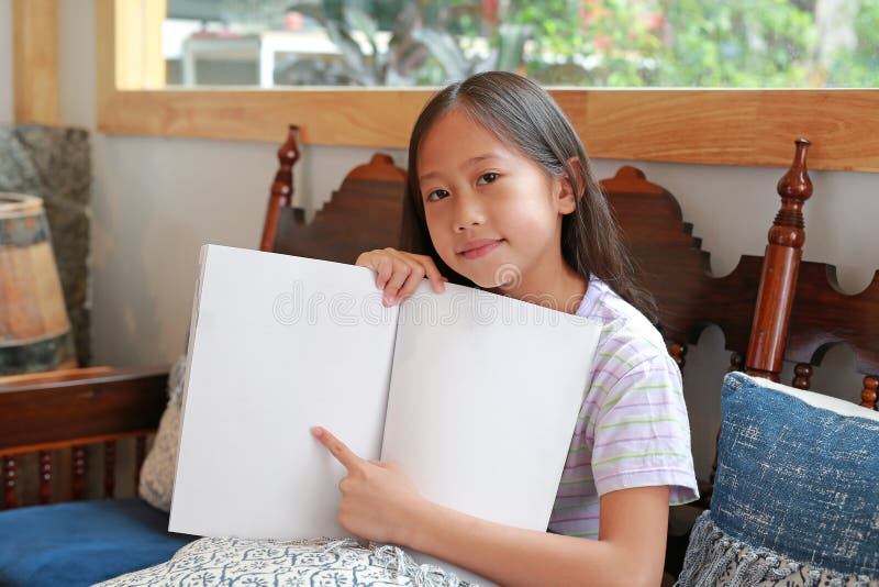 азиатская девушка, держащая книгу и указывая на пустую страницу, сидя на деревянном кресле стоковая фотография