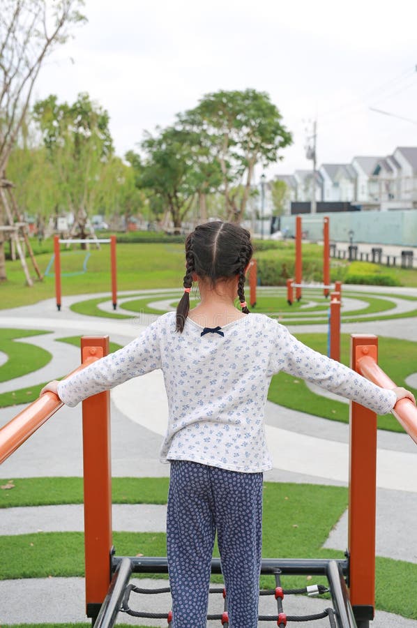 азиатская девушка, играющая на оборудовании на детской площадке. задний вид стоковое изображение