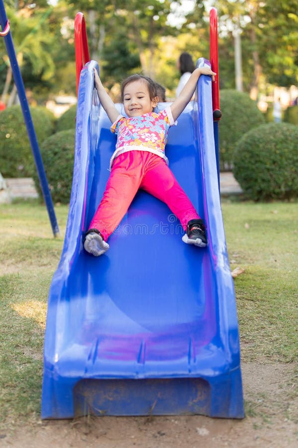 Cute Asian girls with brightly colored floral dresses are playing slider in the amusement playground, and you can notice the smile on her face that spread with happiness. Cute Asian girls with brightly colored floral dresses are playing slider in the amusement playground, and you can notice the smile on her face that spread with happiness