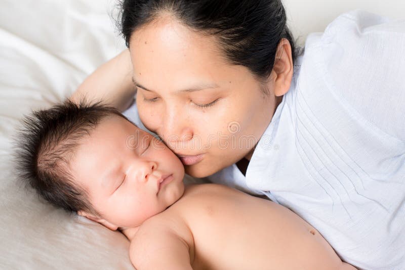 Азиатская мать кладет на кровать с newborn младенцем стоковое изображение