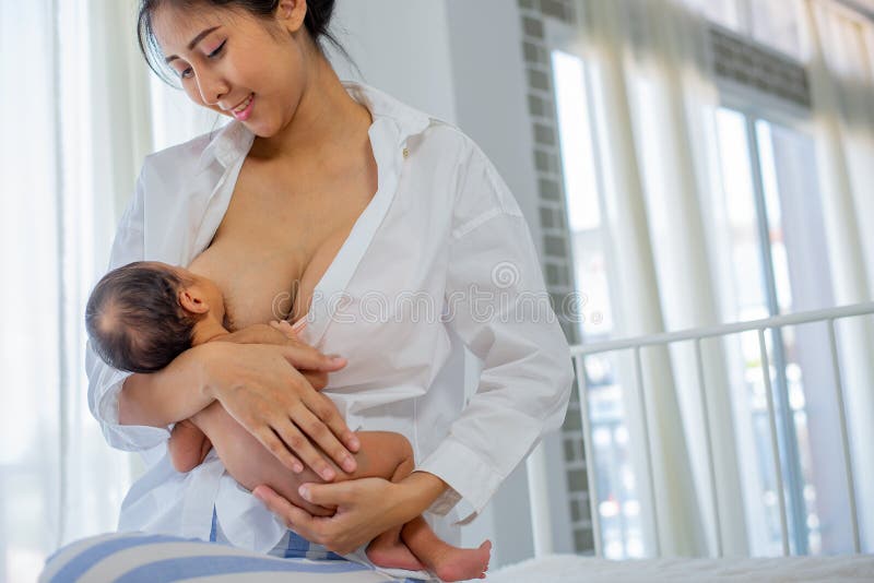 Азиатская мать с усмехаться для того чтобы дать кормить грудью newborn с белой рубашкой и сидеть на предпосылке кровати белой сте стоковое изображение rf Азиатская мать с усмехаться для того чтобы дать кормить грудью newborn с белой рубашкой и сидеть на предпосылке кровати белой сте стоковое изображение rf
