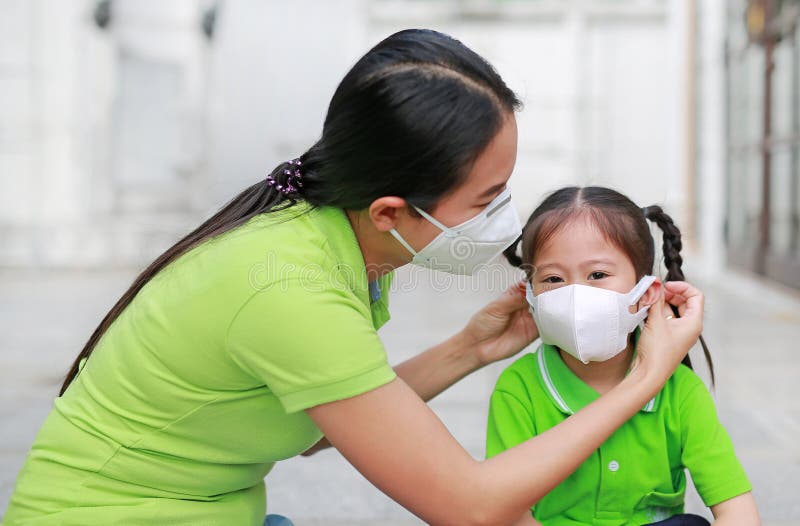 Молодая азиатская мать надевает защитную маску на свою дочь, когда они находятся на улице, чтобы защититься от загрязнения воздуха стоковые фотографии rf