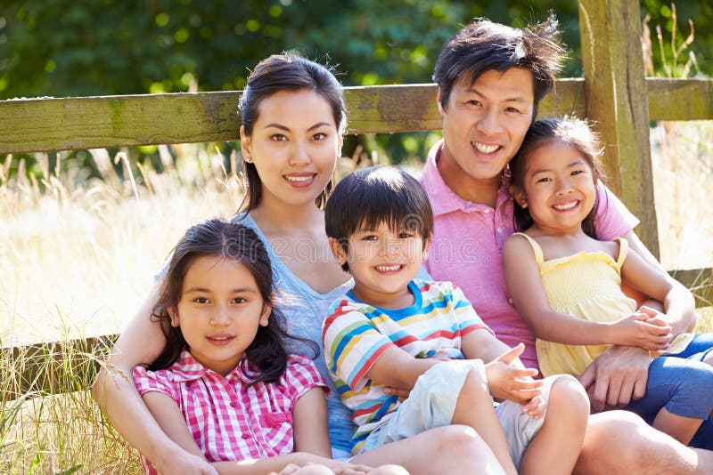 Asian Family Relaxing By Gate On Walk In Countryside Looking At Camera Smiling. Asian Family Relaxing By Gate On Walk In Countryside Looking At Camera Smiling