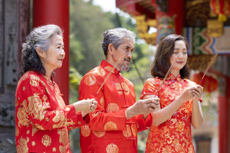 азиатская семья со старшими родителями в красном платье cheongsam qipao предлагает благовония богу предков внутри китайского будди стоковые фото