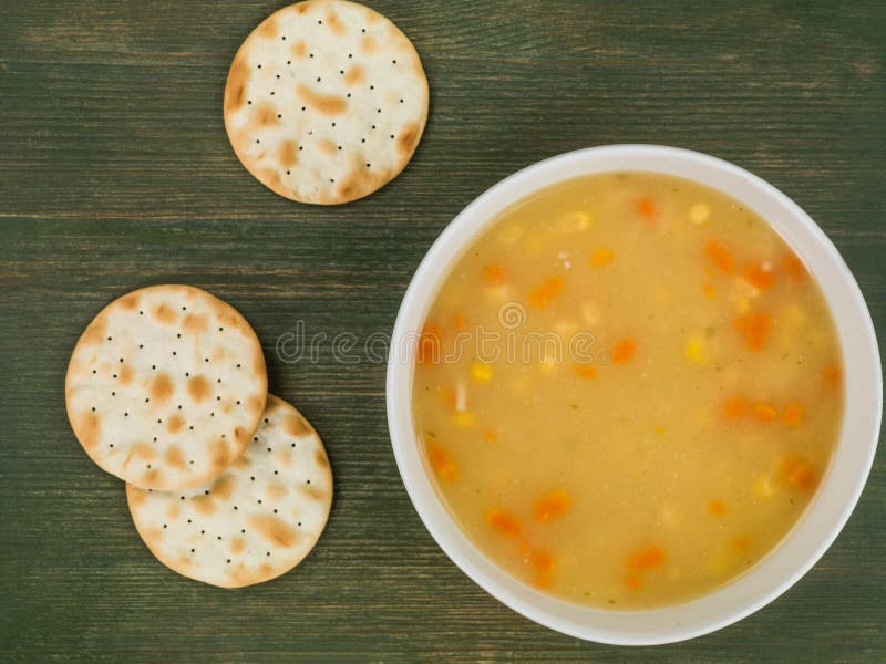 Chicken Sweetcorn and Noodle Soup With Crackers Against a Green Wooden Background. Chicken Sweetcorn and Noodle Soup With Crackers Against a Green Wooden Background