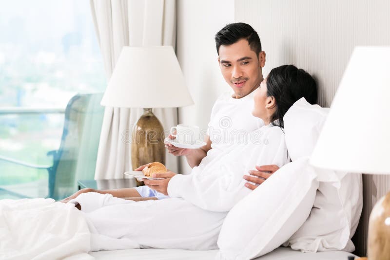 Азиатские пары lounging в кровати стоковые изображения Азиатские пары lounging в кровати стоковые изображения