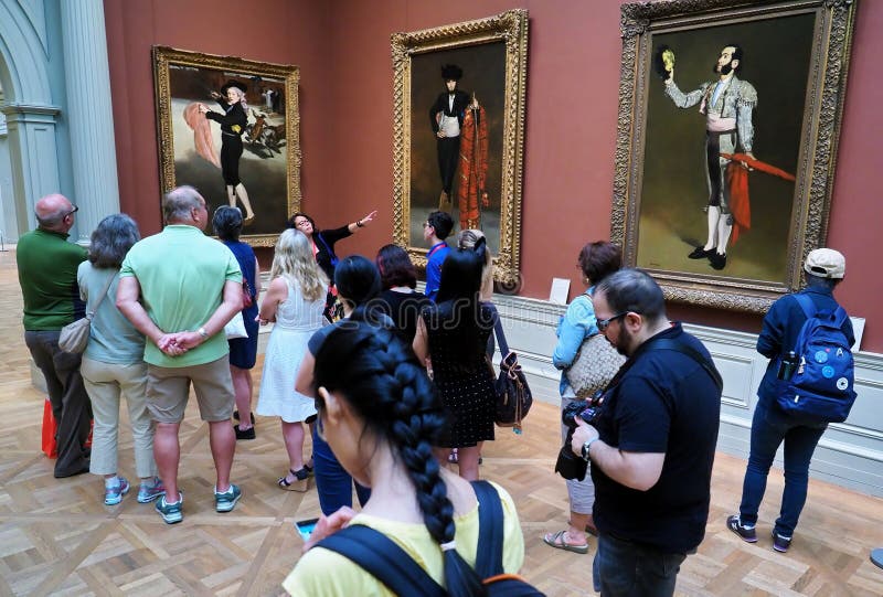 New York City, NY USA. Jul 2017. Asian American tour guide giving a group of visitors an educational briefing on some of the exotic paintings at The MET. New York City, NY USA. Jul 2017. Asian American tour guide giving a group of visitors an educational briefing on some of the exotic paintings at The MET