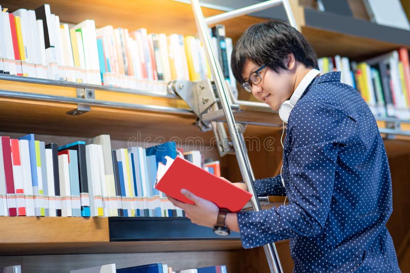 Азиатский парень выбирая книгу от книжных полков в библиотеке стоковые фото Азиатский парень выбирая книгу от книжных полков в библиотеке стоковые фото