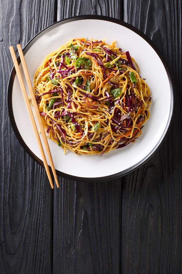 Asian Noodle Salad with thinly sliced red cabbage, julienned carrots in spicy peanut dressing close-up in a plate on the table. Vertical top view from above. Asian Noodle Salad with thinly sliced red cabbage, julienned carrots in spicy peanut dressing close-up in a plate on the table. Vertical top view from above