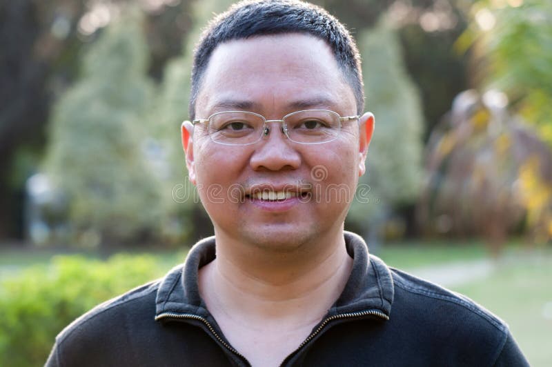 One asian mid-adult man looks straight at camera in outdoor, green background. One asian mid-adult man looks straight at camera in outdoor, green background