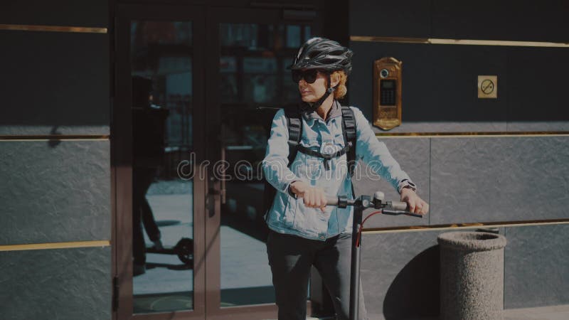 Активная зрелая женщина в стильных одежде работает в службе доставки на электрическом мотороллере. Женщины среднего возраста на pu сток-видео