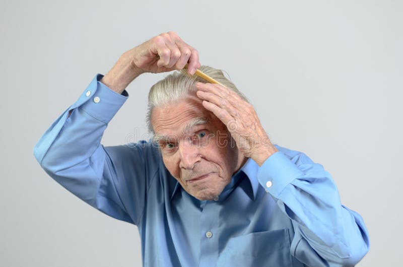 Active healthy elderly man wearing a clean blue shirt while combing his hair with a plastic comb, part of daily routine, portrait with copy space on gray. Active healthy elderly man wearing a clean blue shirt while combing his hair with a plastic comb, part of daily routine, portrait with copy space on gray