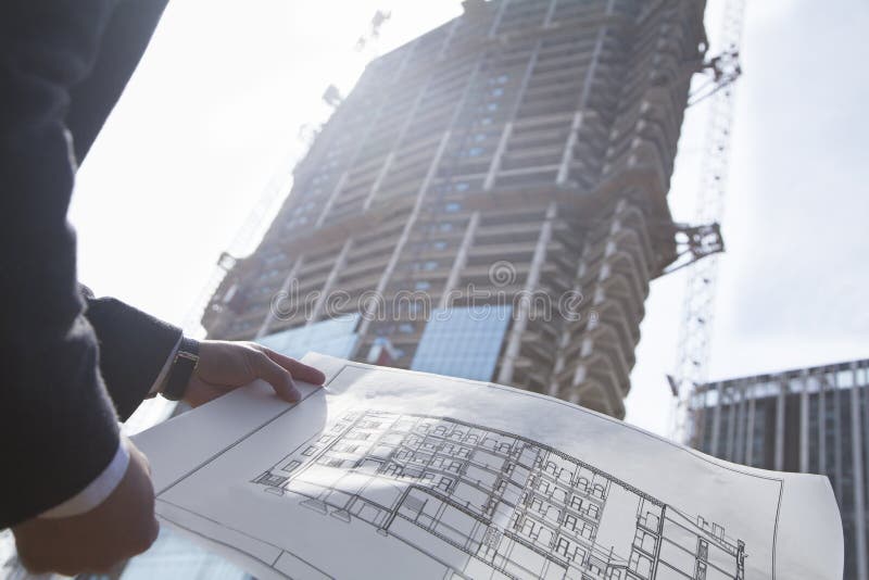 Architect holding blueprint of building at a construction site, midsection. Architect holding blueprint of building at a construction site, midsection